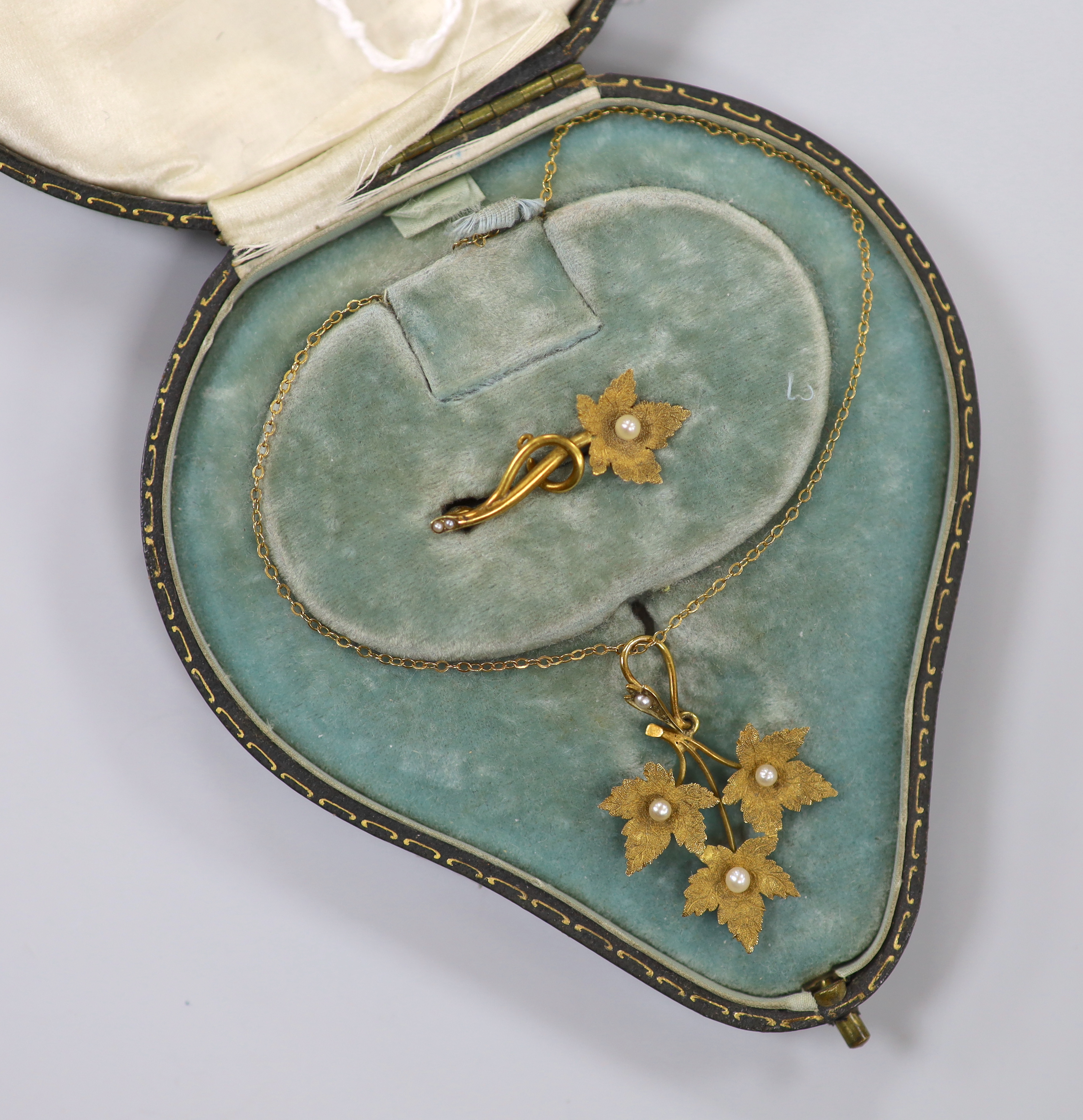 A late Victorian 15ct and seed pearl set leaf pendant, 36mm, on a 9ct chain, 39mm and a matching brooch, in fitted leather case, gross weight 4.6 grams.